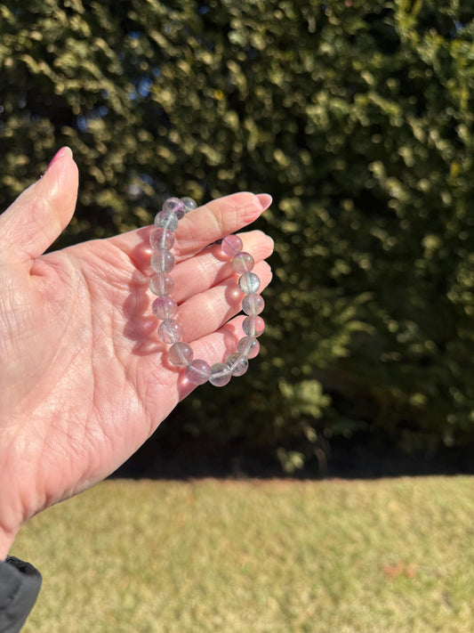 May include: A bracelet made of iridescent, light green and pink beads. The beads are round and smooth, and the bracelet is strung on a clear elastic cord.