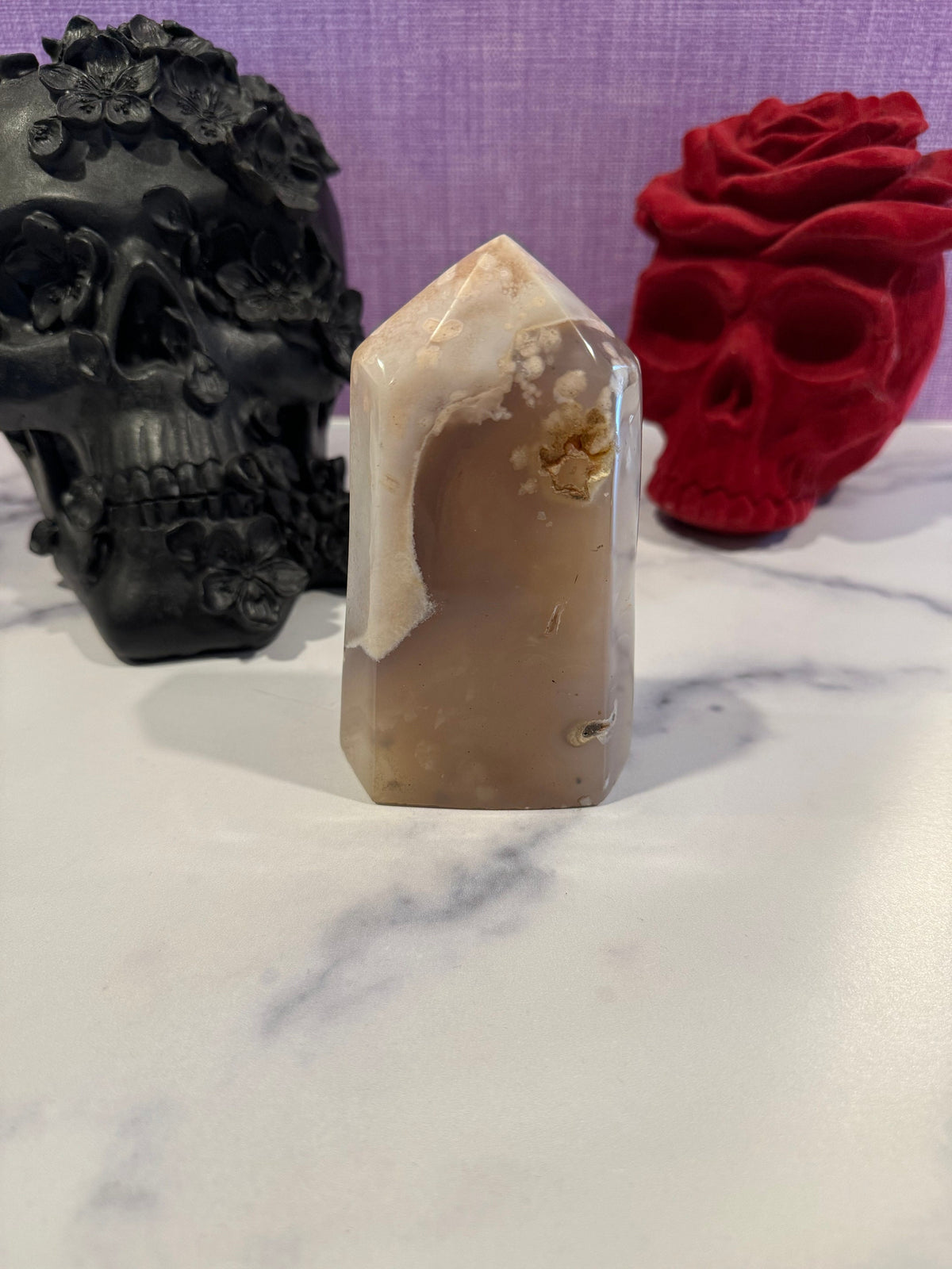 May include: A light brown agate crystal point with white and brown banding. The crystal is sitting on a white surface.